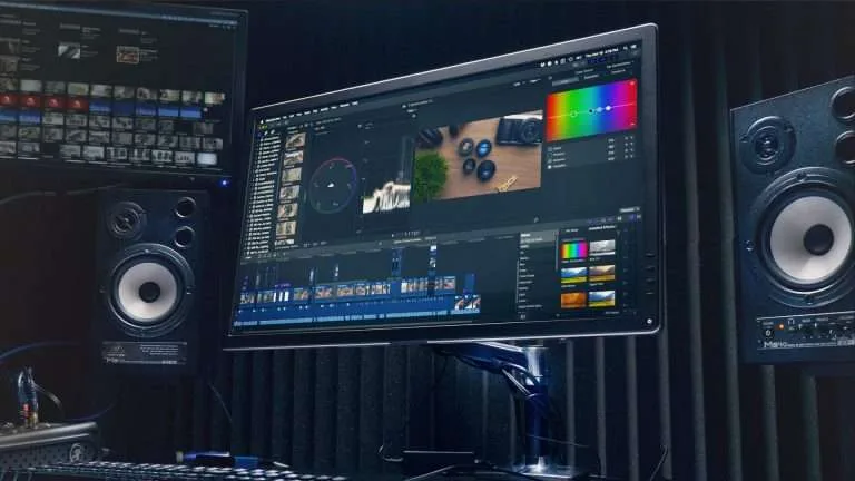 Estúdio de edição de vídeo com monitor mostrando ferramentas de correção de cor e timeline de edição. Equipado com alto-falantes de áudio profissional.